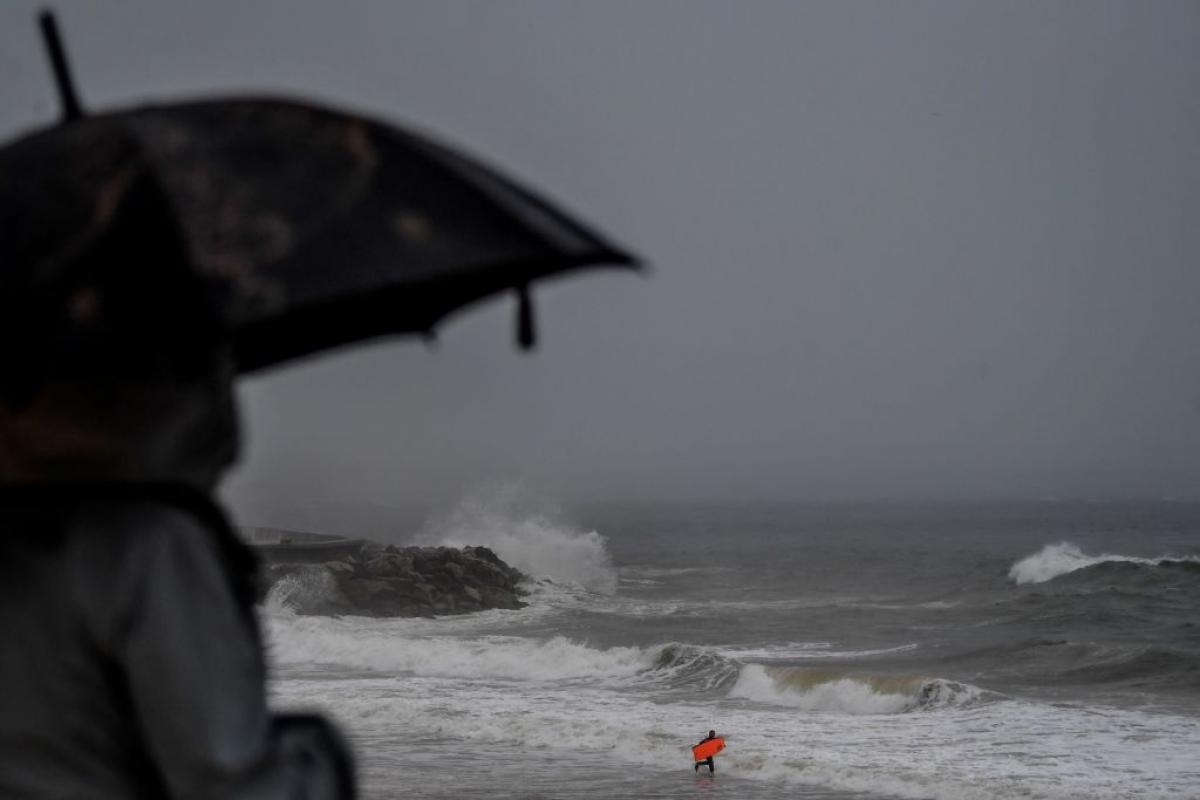 Una persona se cubre bajo un paraguas mientras ve una playa