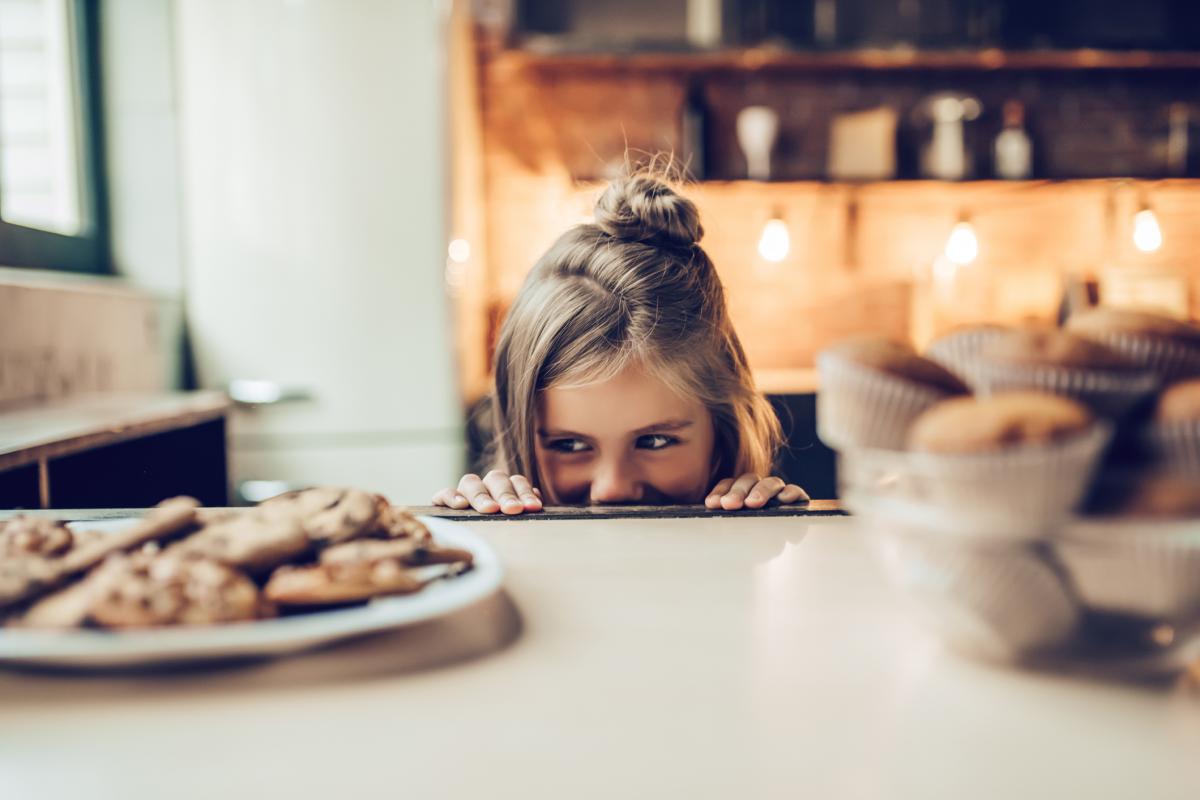 Imagen de archivo de una pequeña observando con interés un plato de galletas.