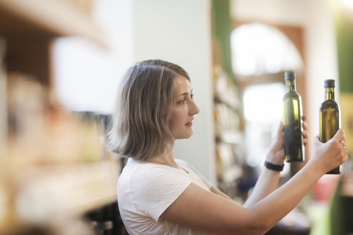Imagen de archivo de una mujer comparando dos botellas de aceite de oliva en un supermercado.