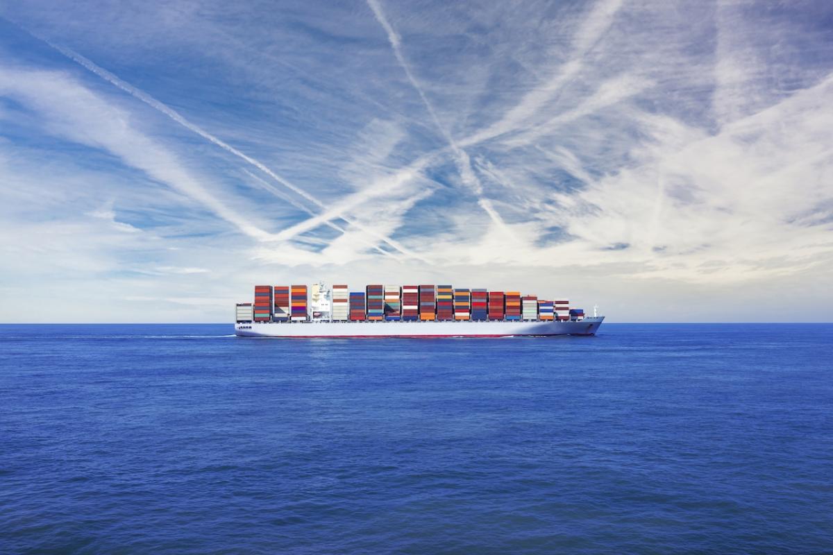 Un buque cargado de contenedores navega bajo un cielo lleno de nubes bajas.