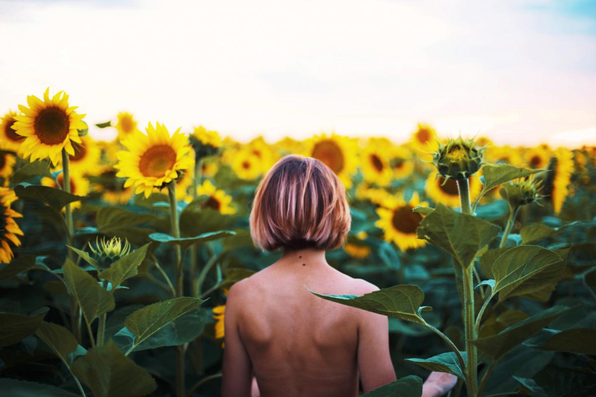 Imagen de una mujer caminando desnuda entre girasoles.