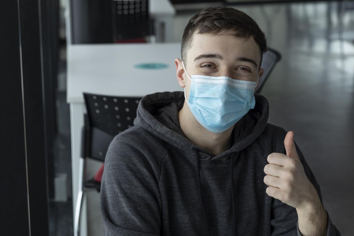 Imagen de archivo con un joven con mascarilla haciendo un gesto afirmativo con el pulgar.