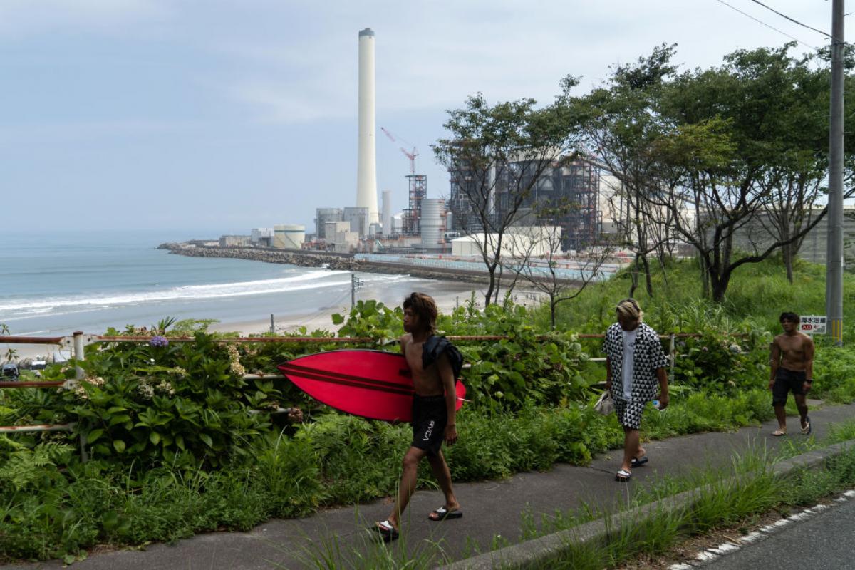 Un grupo de surfistas pasa por delante de la central nuclear de Fukushima.