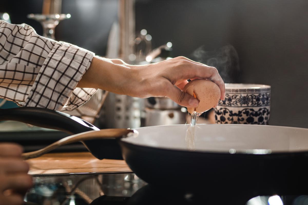Una persona cascando un huevo en el borde de la sartén.