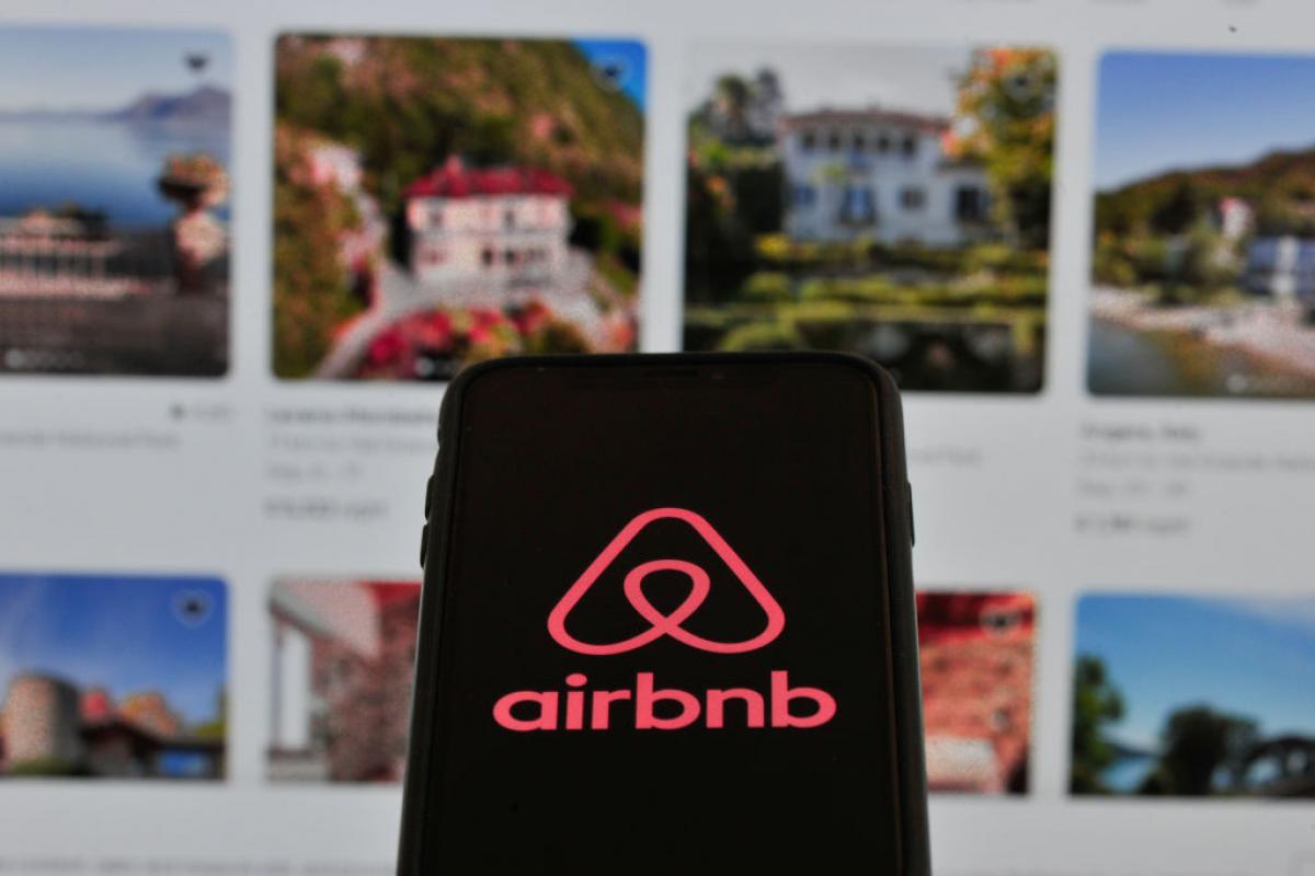 El logotipo de Airbnb en un teléfono móvil con la oferta de pisos turísticos al fondo.