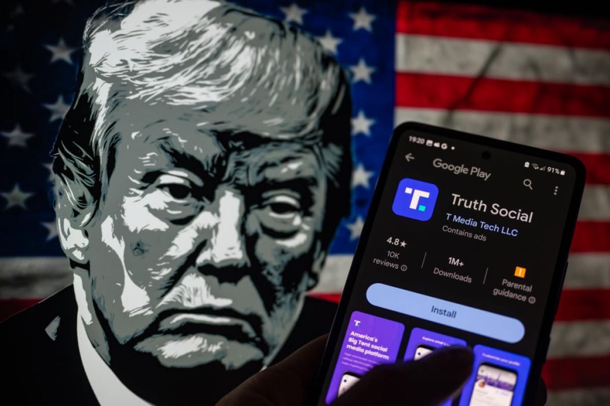 La red social Truth Social en la pantalla de un móvil con el rostro de Trump, dibujado al fondo.