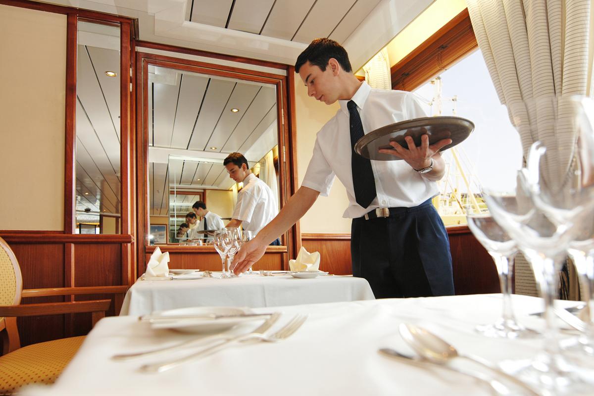 Una trabajador colocando la mesa de un restaurante en un crucero.