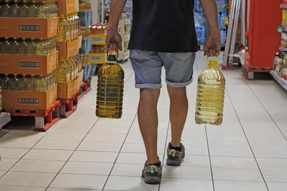 Un hombre lleva dos garrafas de aceite en un supermercado.