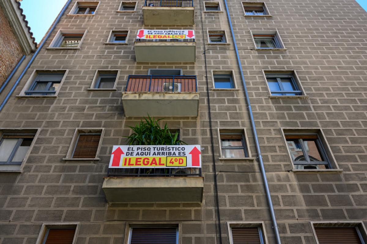 Carteles de protesta señalando viviendas turísticas ilegales, en un edificio cercano a