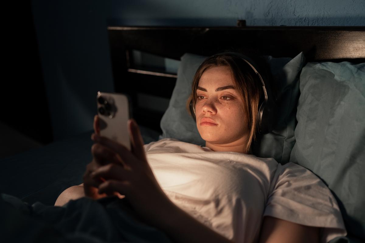 Imagen de archivo de una mujer joven en la cama con un móvil.