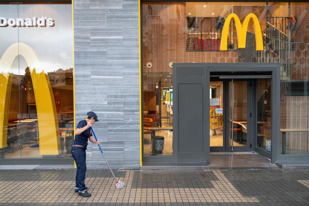 Una trabajadora de McDonald's limpia la acera frente a un restaurante de la cadena en Barcelona.