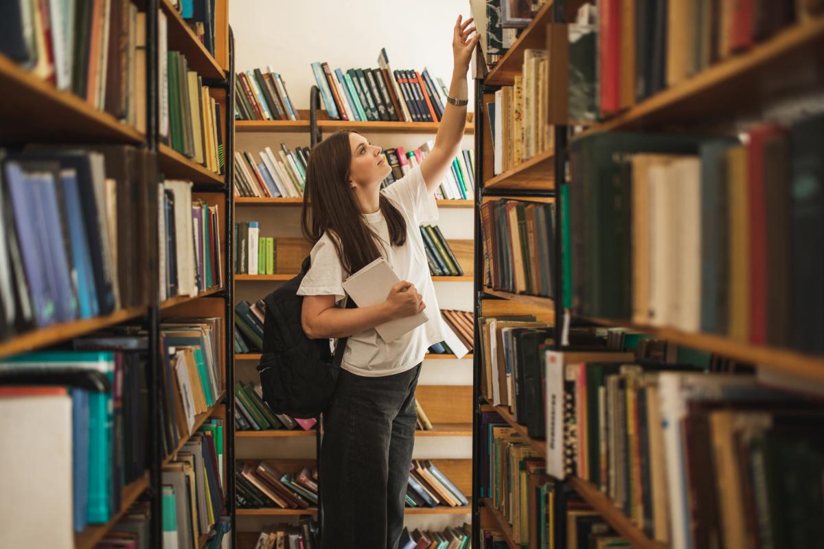 Una mujer cogiendo un libro en la biblioteca.