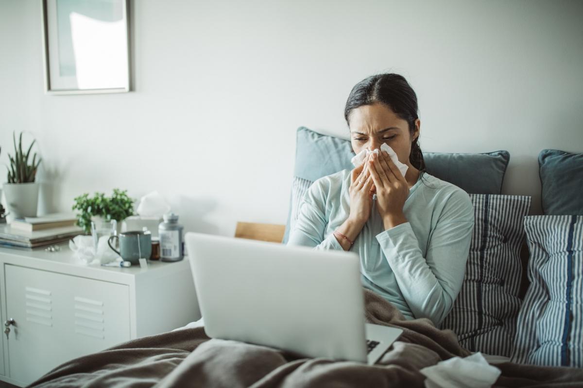Una mujer con gripe, en cama con el ordenador del trabajo.