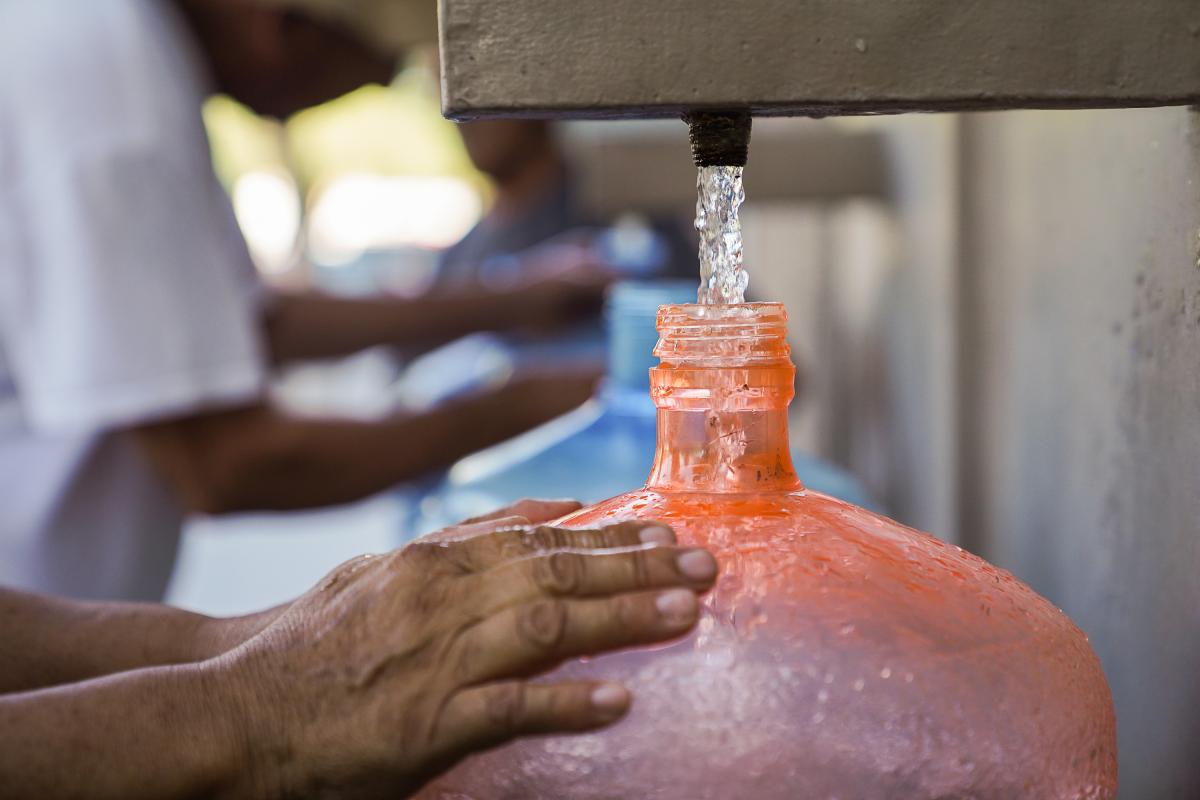 Una persona llenando un recipiente con agua.