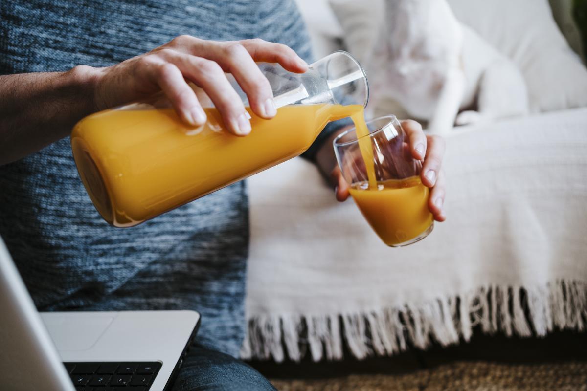Un hombre echando zumo de naranja en un vaso.