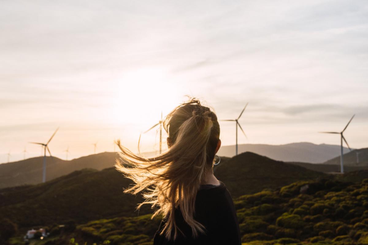 Imagen de archivo de una persona contemplando un atardecer con aerogeneradores al fondo.