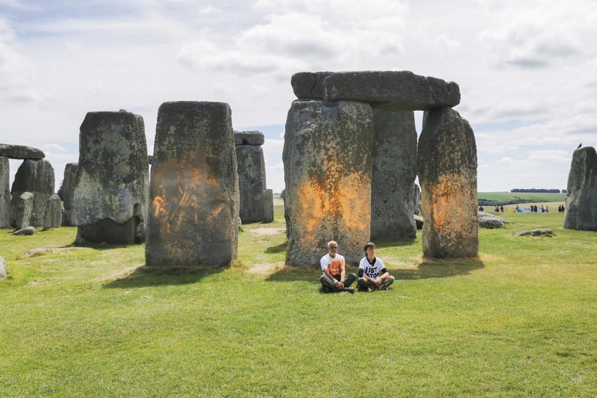 Los dos activistas de Just Stop Oil sentados ante el monumento de Stonehenge tras rociar al pintura naranja sobre las piedras.