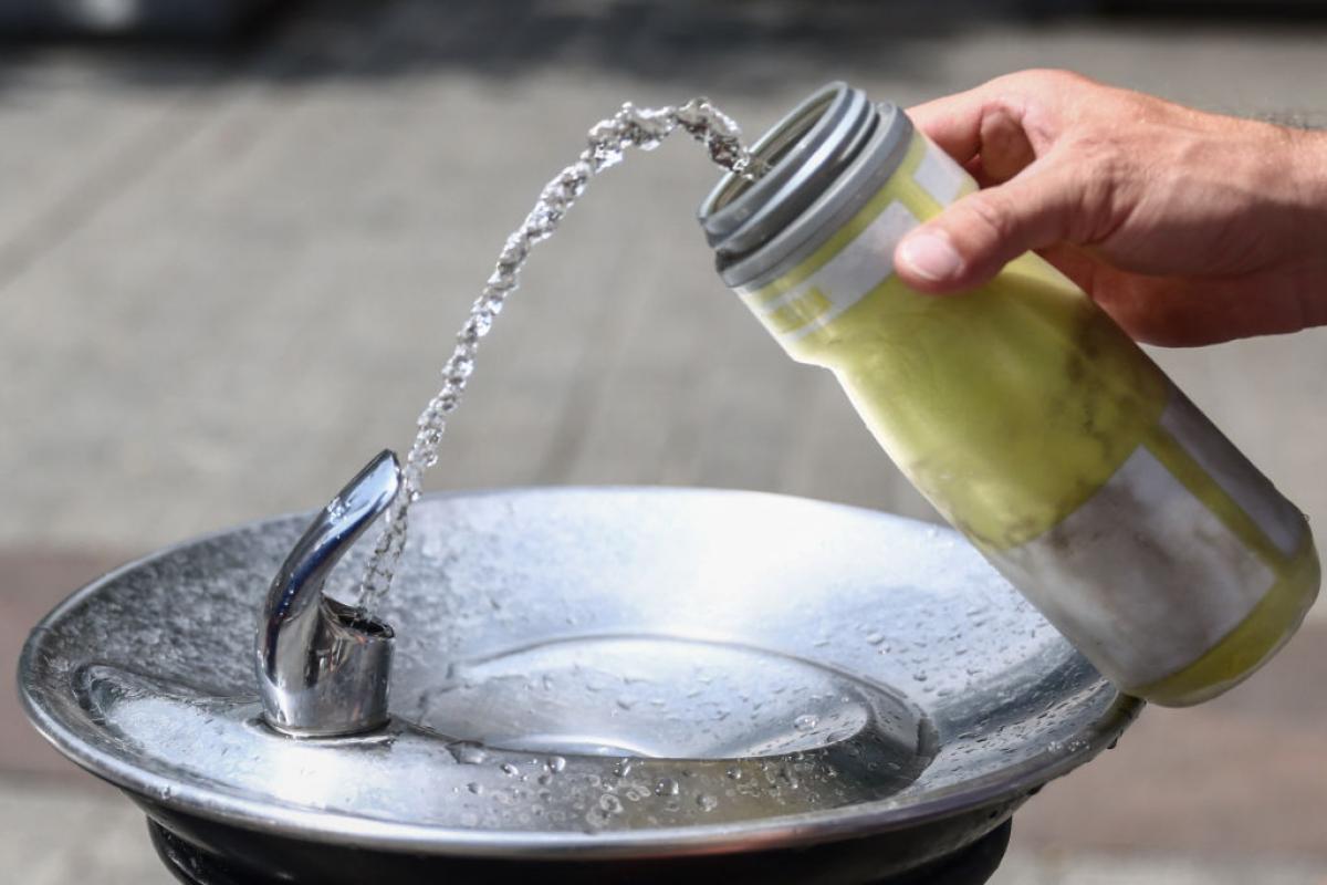 Una persona llena de agua su botella en una fuente pública.