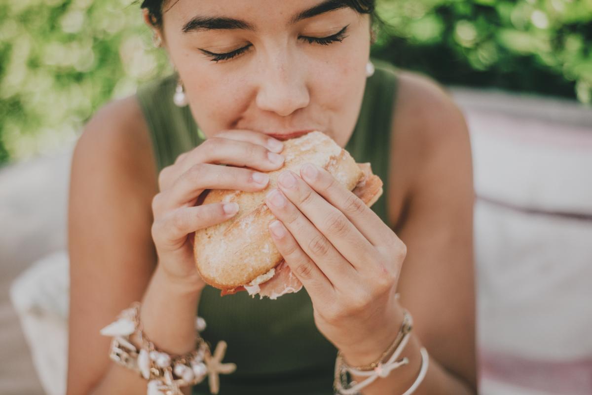 Una mujer pegándole un bocado a su bocadillo.