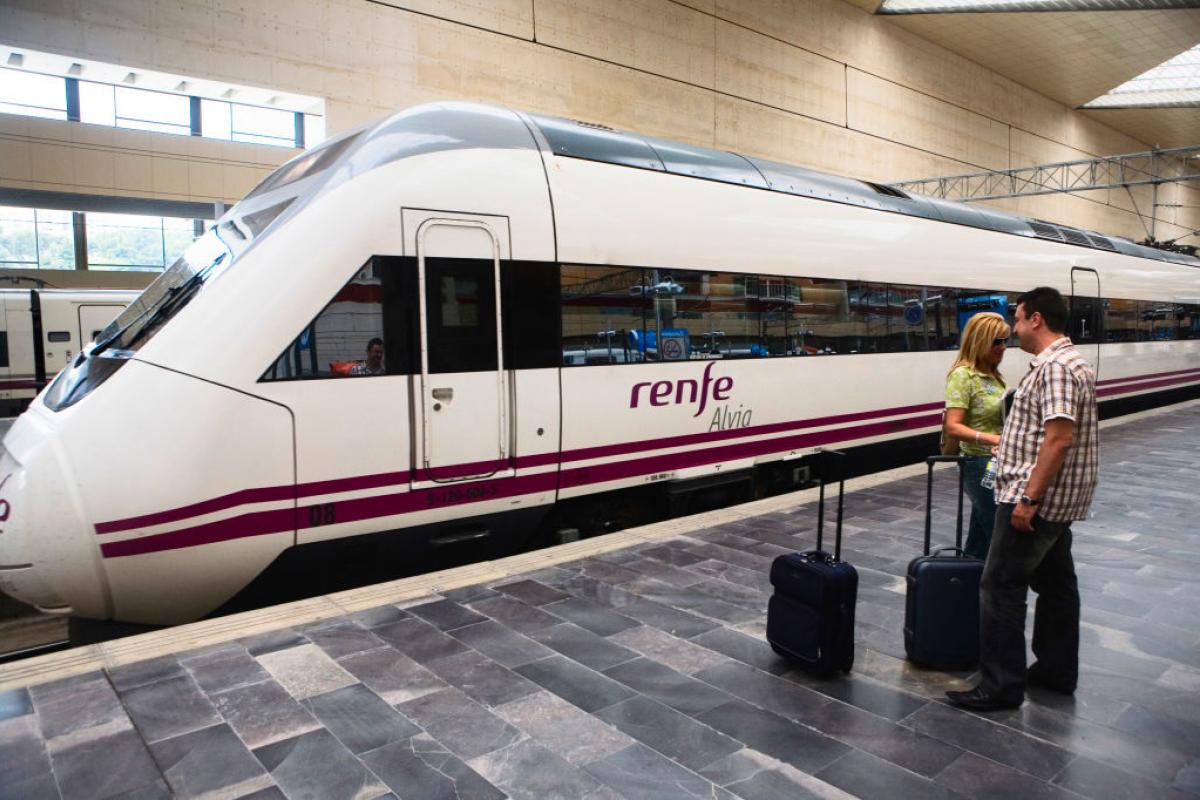 Dos personas pasan con su maletas por delante de un tren de Renfe, en Zaragoza.