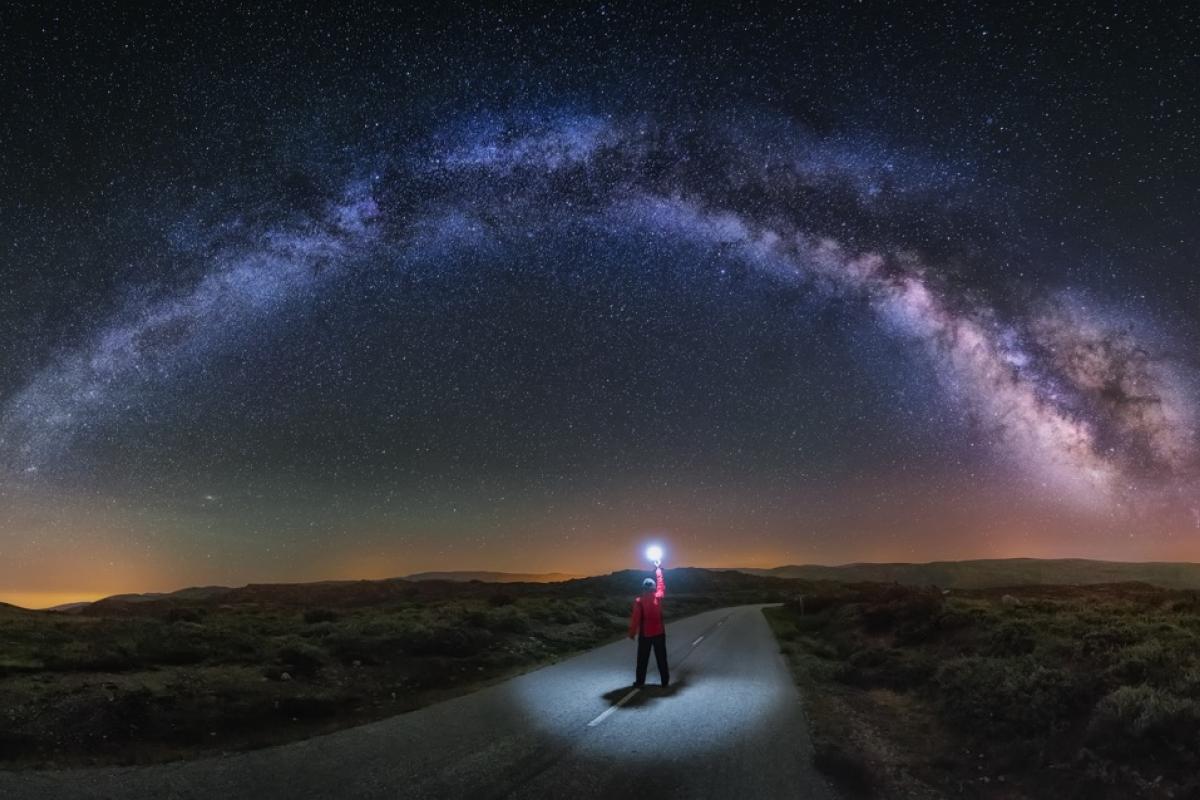 Un joven observa la Vía Láctea en A Veiga, Ourense, y alumbra el camino con una linterna.