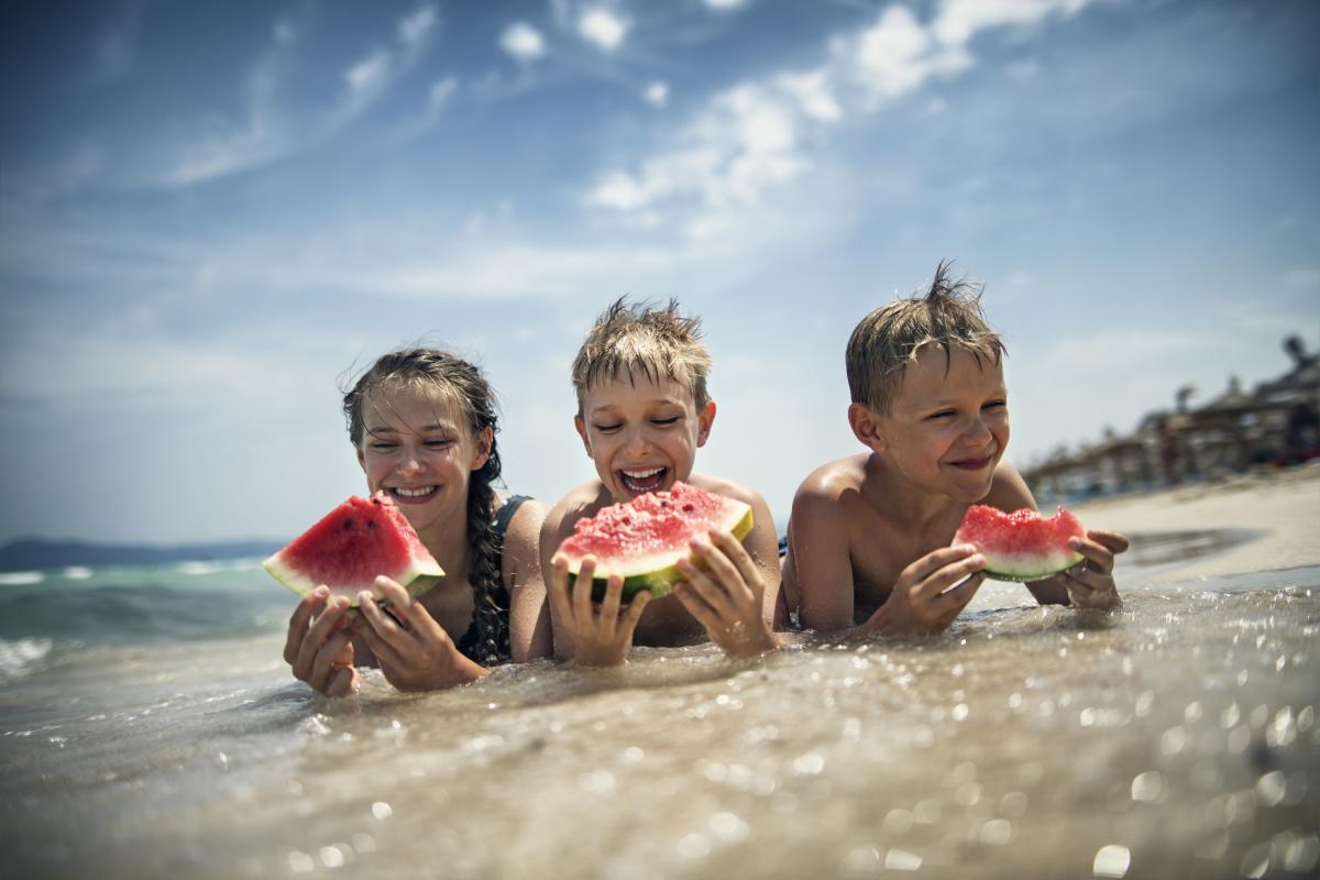 Unos niños comiendo sandía en la playa.