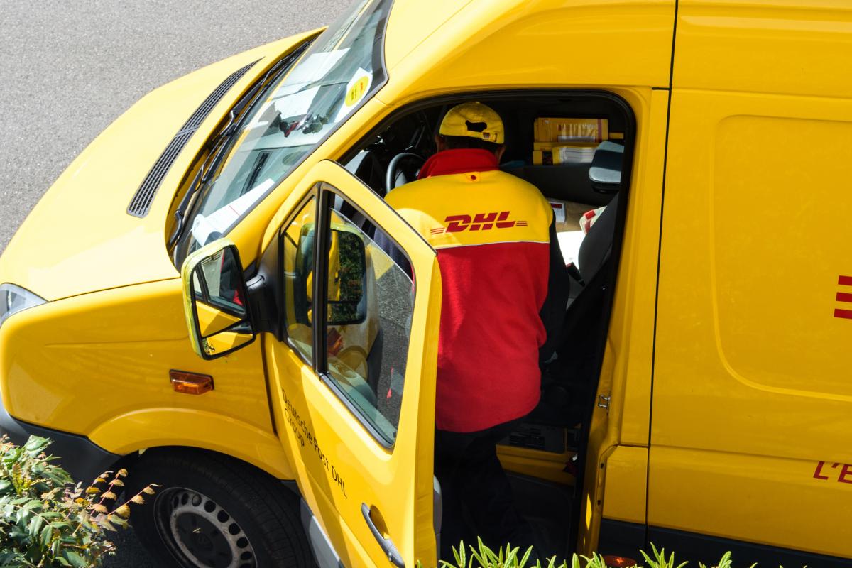 El mensajero ingresa a la furgoneta de entrega amarilla de DHL después de entregar el paquete