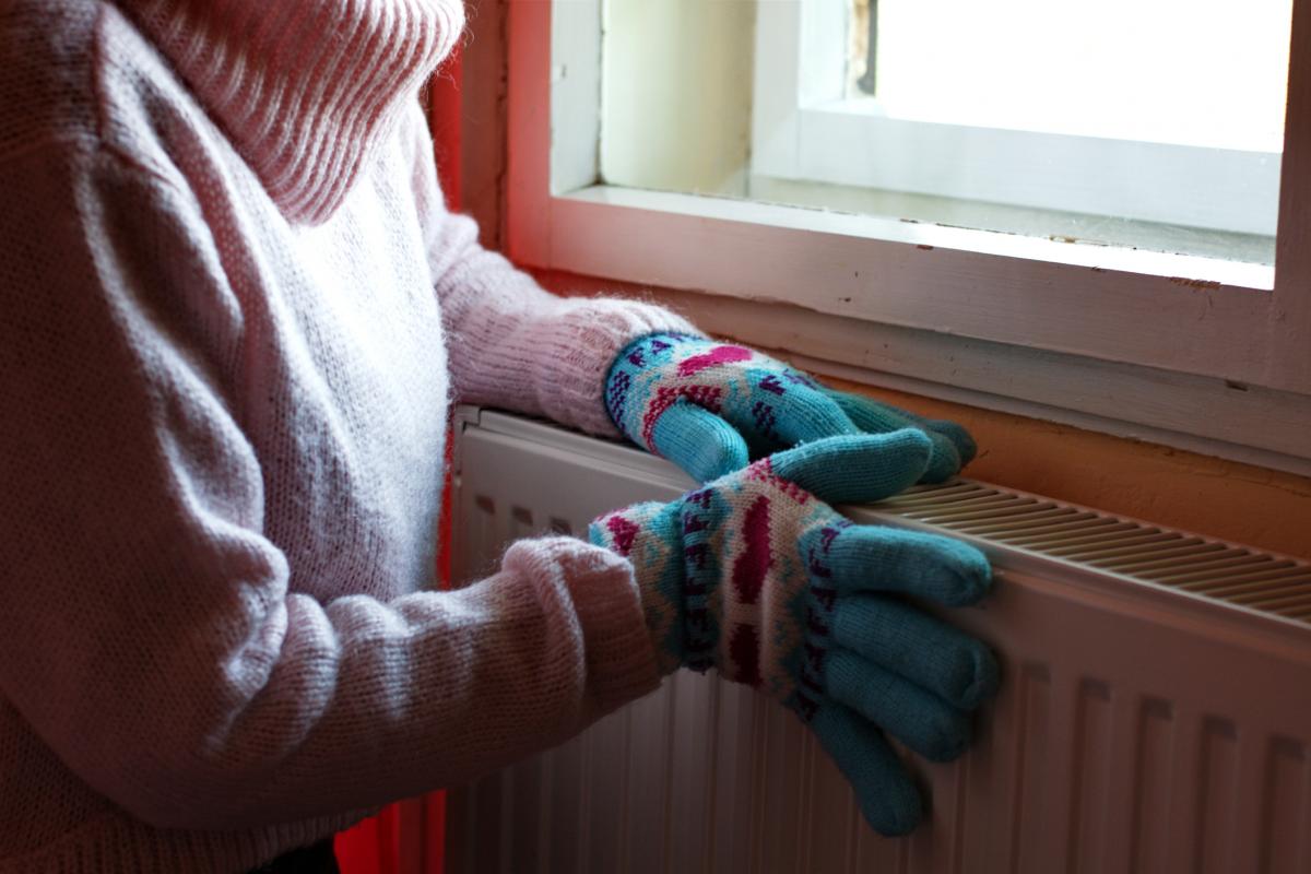Una persona con guantes se agarra a un radiador para no pasar frío en casa.