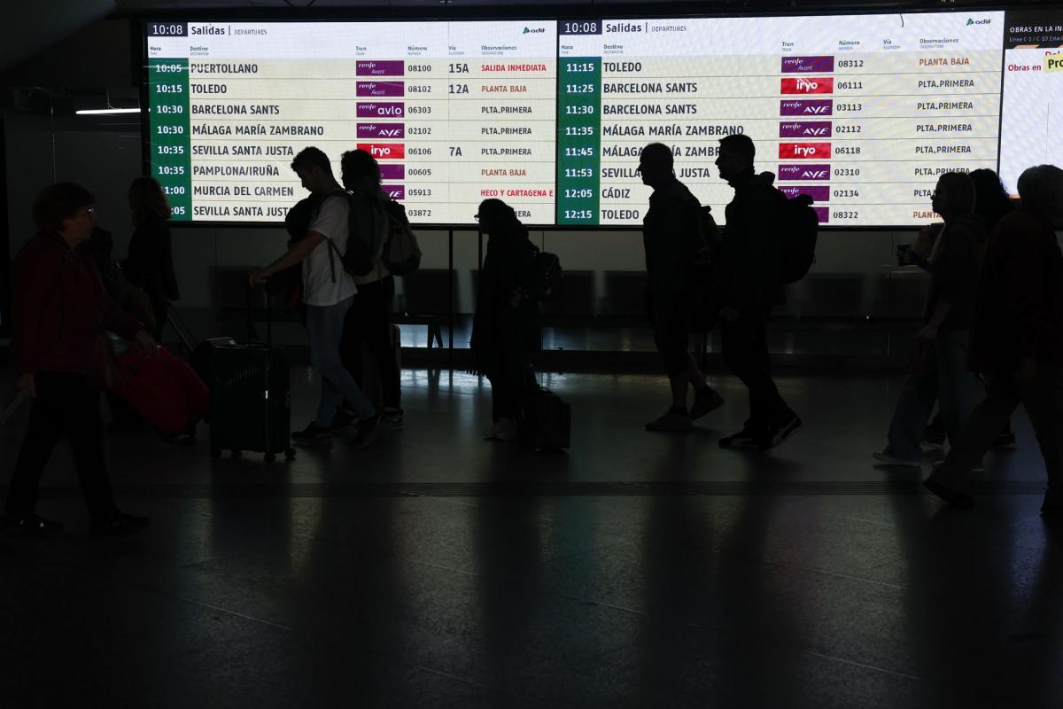 Varios viajeros hacen cola ante el acceso a uno de los andenes en la estación de Atocha.