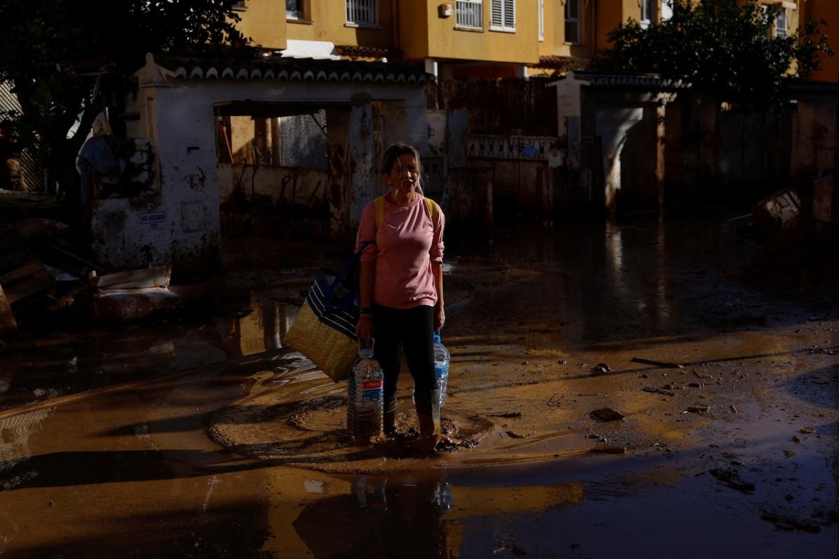 Una mujer que lleva agua embotellada camina por el barro en una calle de Alfafar.