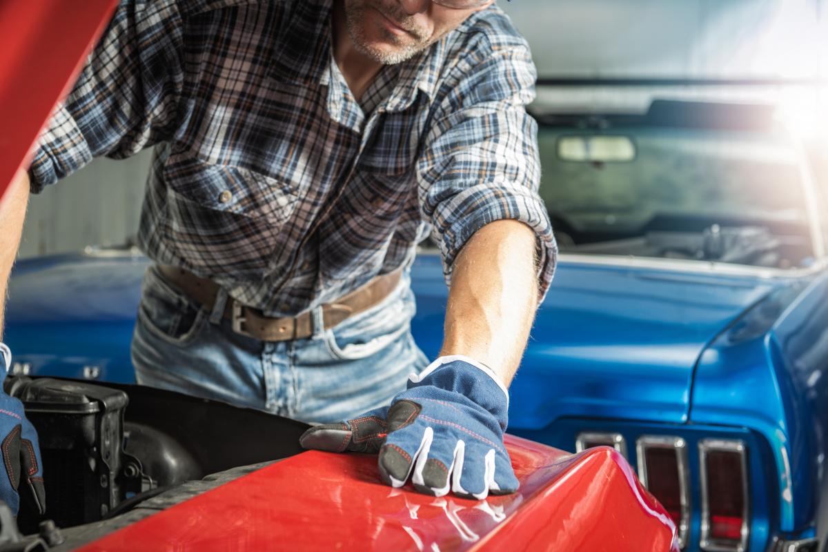 Imagen de un hombre inspeccionando el motor de un deportivo clásico rojo.