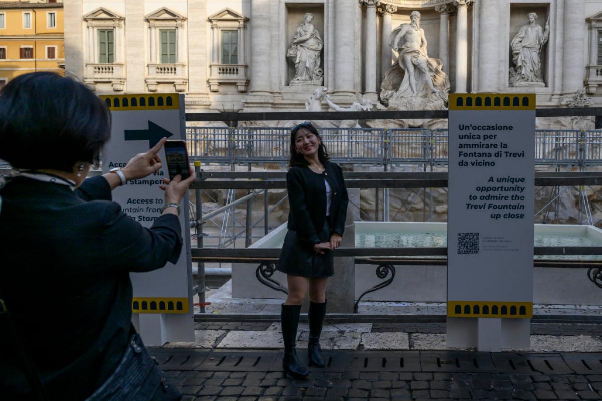 Una turista se fotografía con la pasarela temporal de la Fontana di Trevi de fondo.
