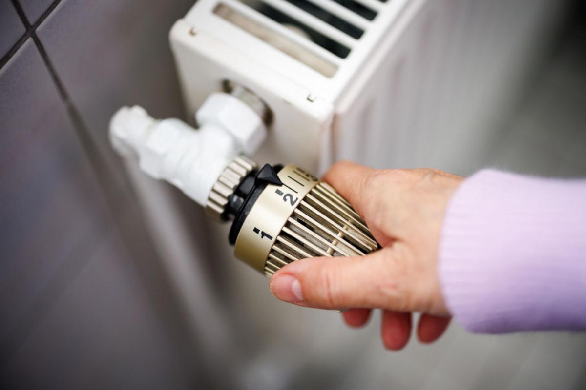 Una mujer sube la temperatura de un radiador conectado a una calefacción de gas.