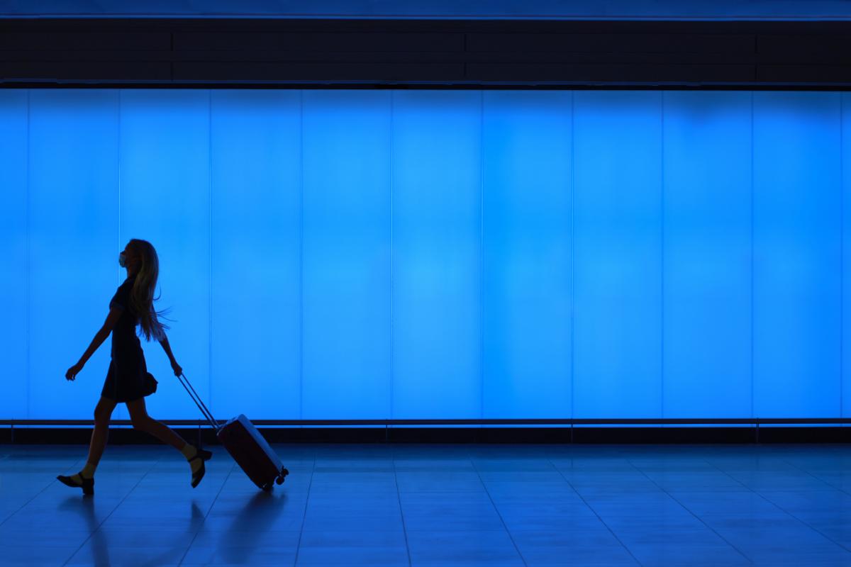 Imagen de la silueta de una mujer, andando en un aeropuerto con una maleta.