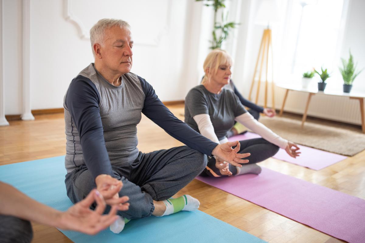 Un hombre mayor medita junto a una mujer mayor durante una clase de yoga en un estudio de yoga.