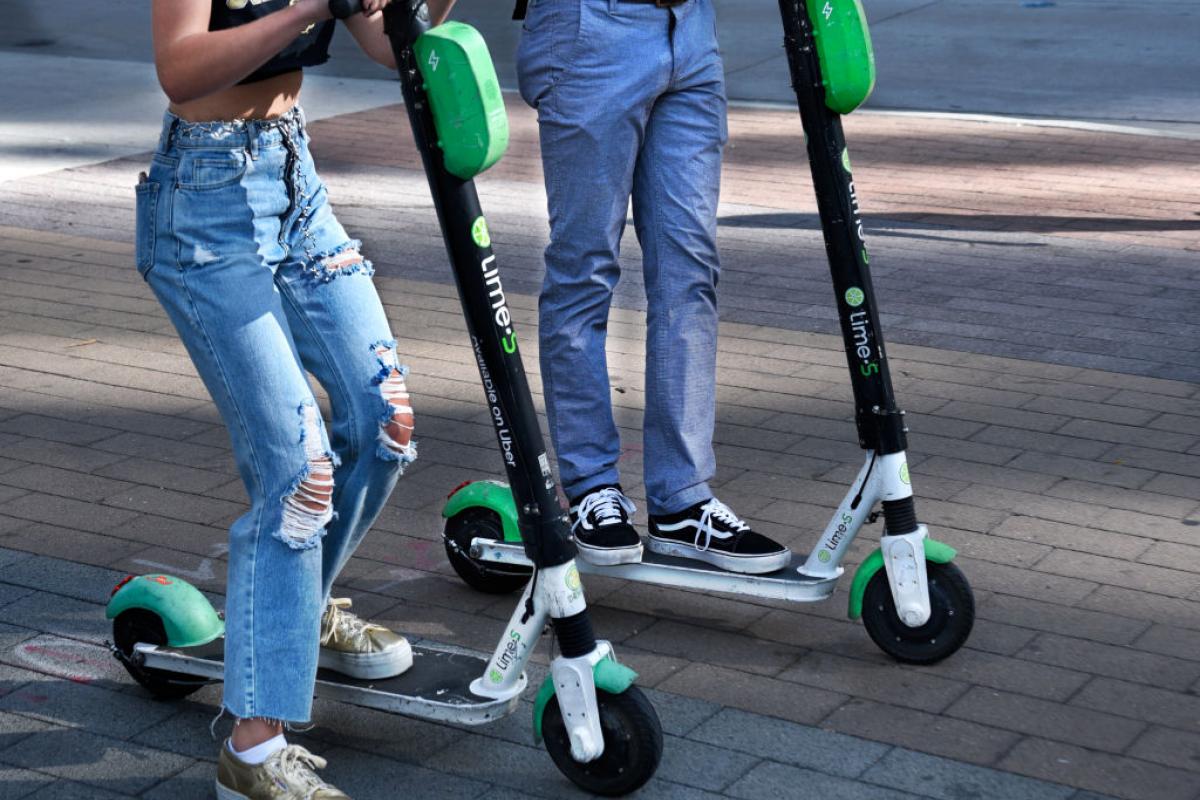 Dos adolescentes se mueven en un patinete eléctrico alquilado.