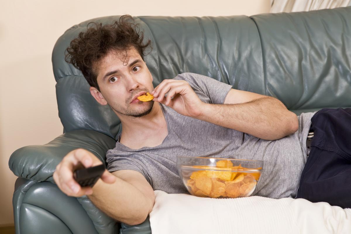 Un hombre comiendo chucherías mientras ve el fútbol.