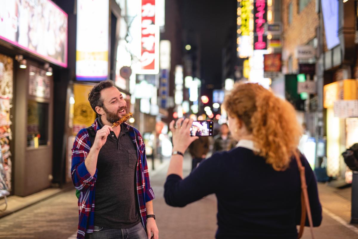 Dos turistas prueban comida callejera en una calle de Tokio.