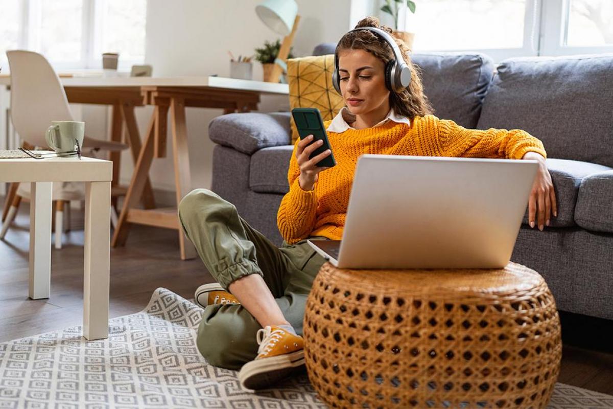 una chica sentada con su móvil, auriculares y ordenador portátil