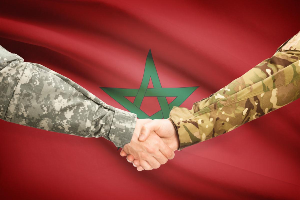 Ilustración digital de dos hombres uniformados estrechándose la mano ante la bandera de Marruecos.