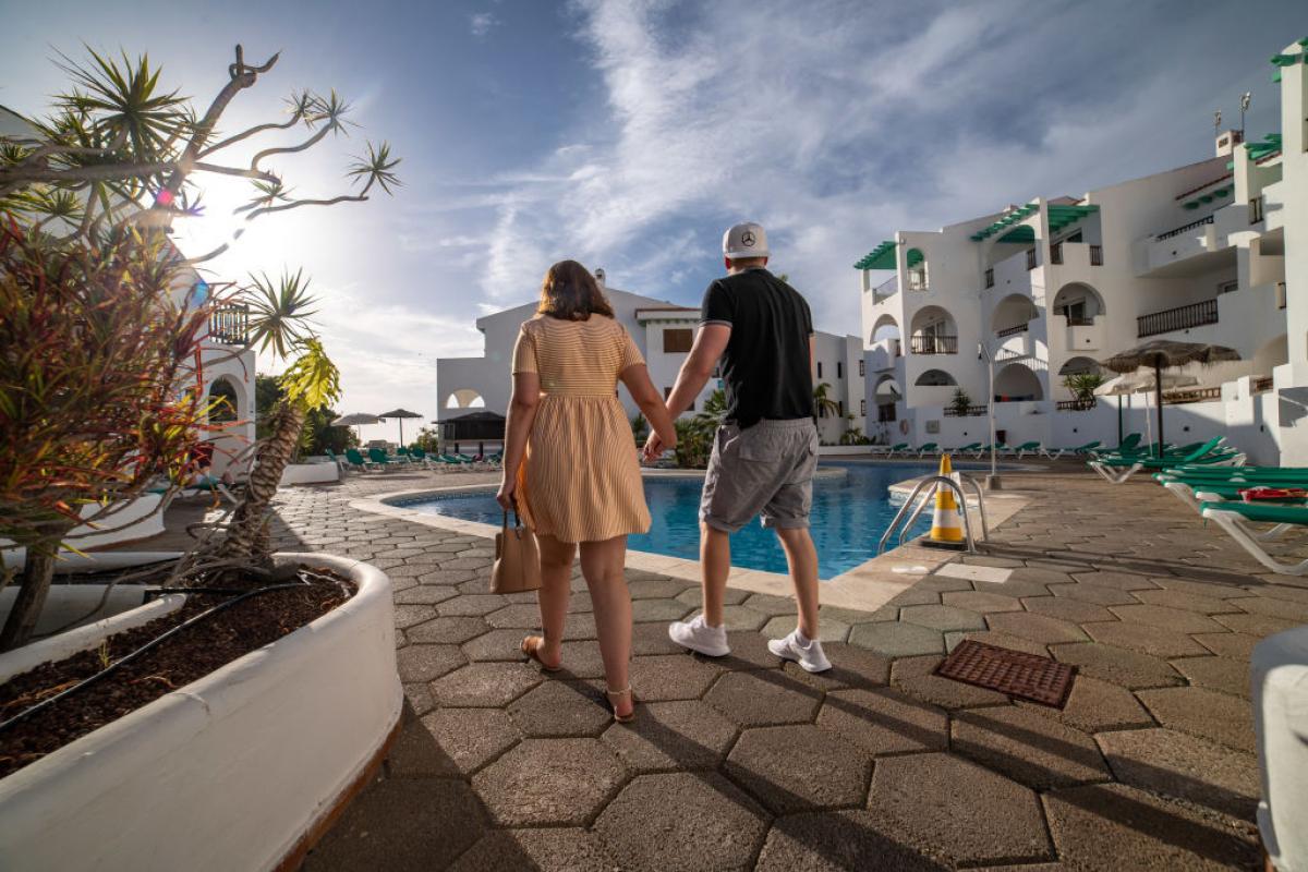 Una pareja de turistas pasa junto a la piscina de una urbanización en Callao Salvaje, Tenerife.