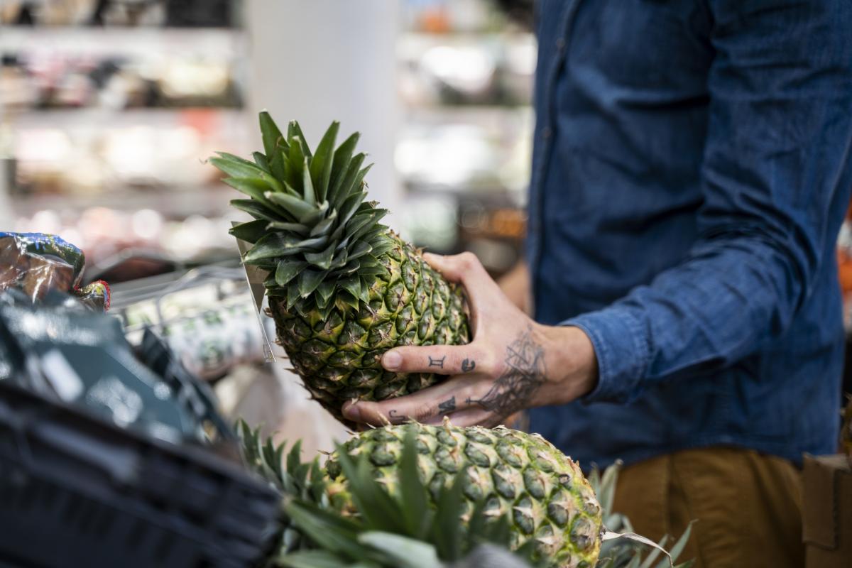 Una persona eligiendo una piña en un supermercado.