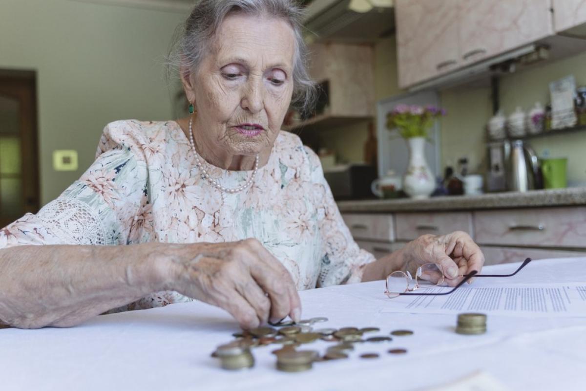 Jubilada contando monedas sobre la mesa mientras revisa papeles en su cocina.