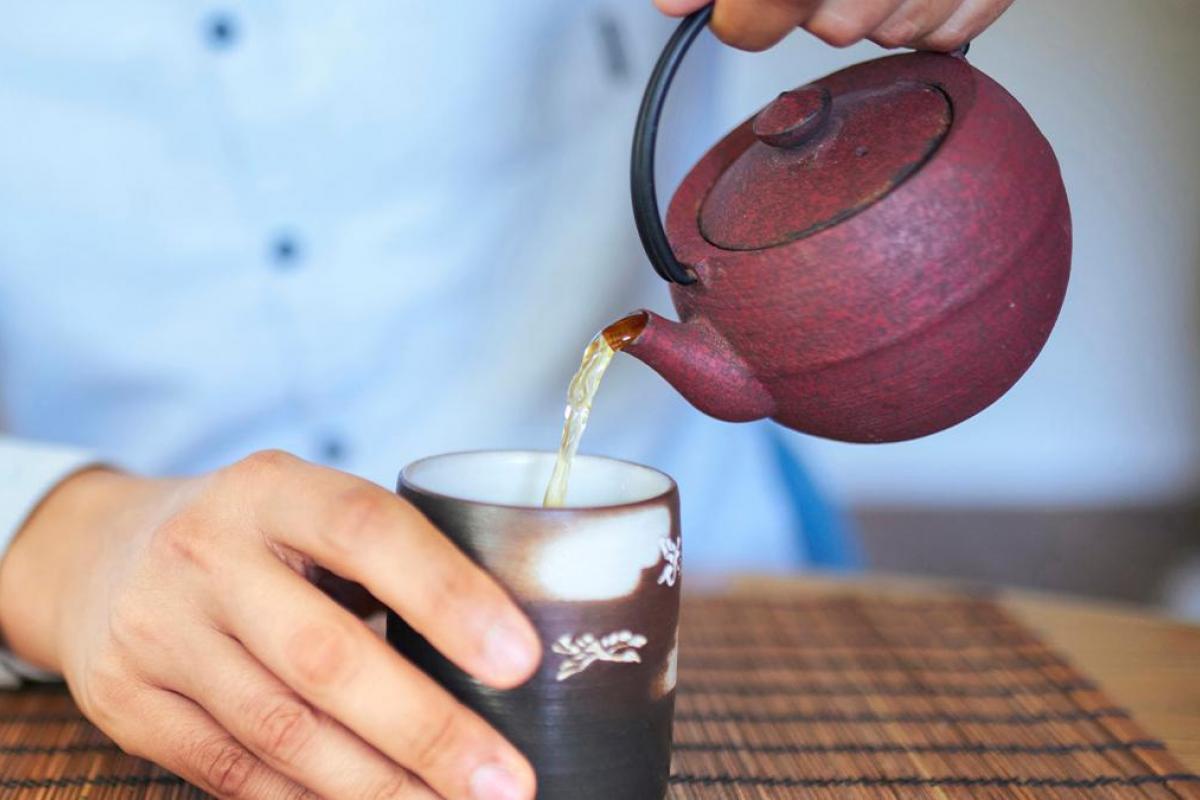 Un hombre echando té en un vaso desde una tetera