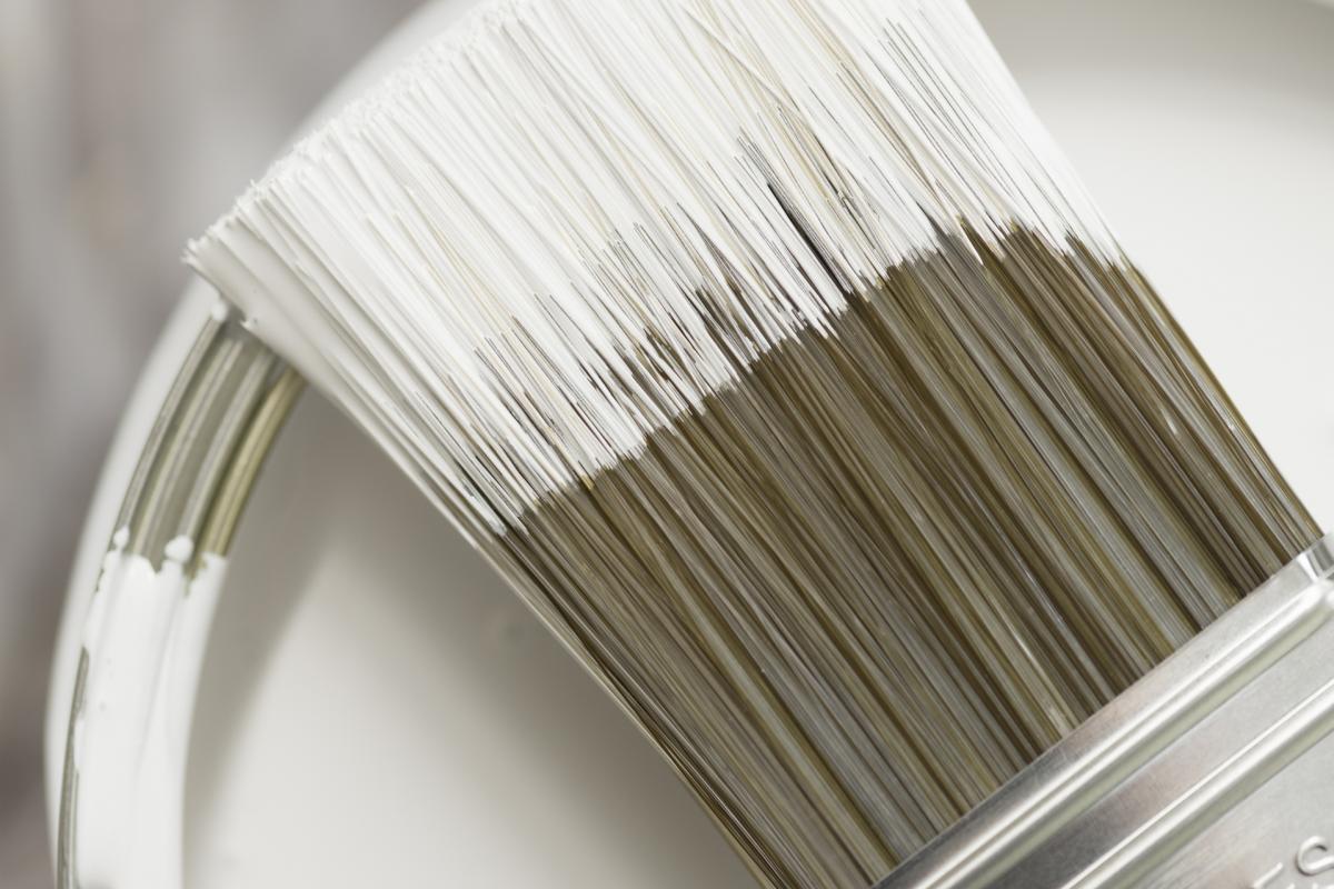 Imagen de archivo de un cubo de pintura blanca y una brocha.