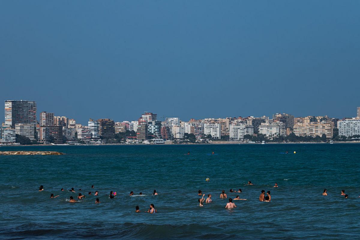 Turistas y vecinos disfrutan en la playa de El Postiguet de un día soleado y calor.
