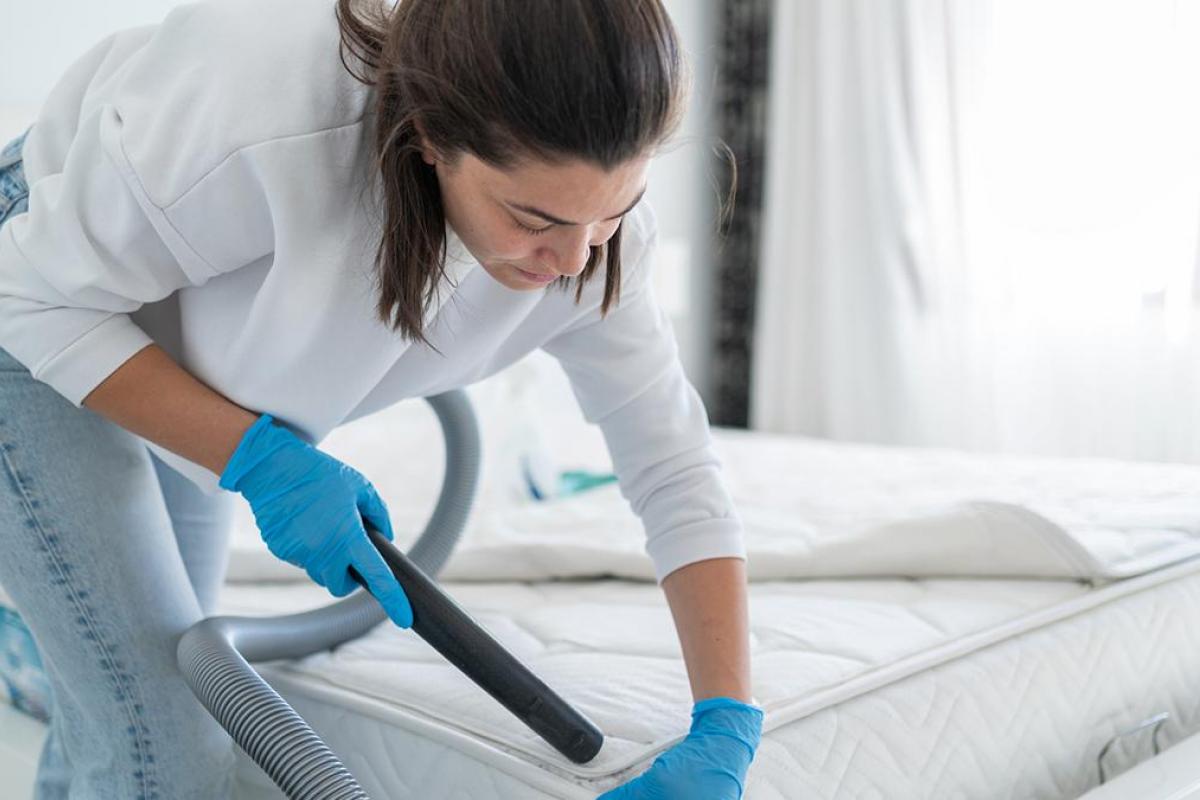una mujer limpiando el colchón con unas aspiradora.