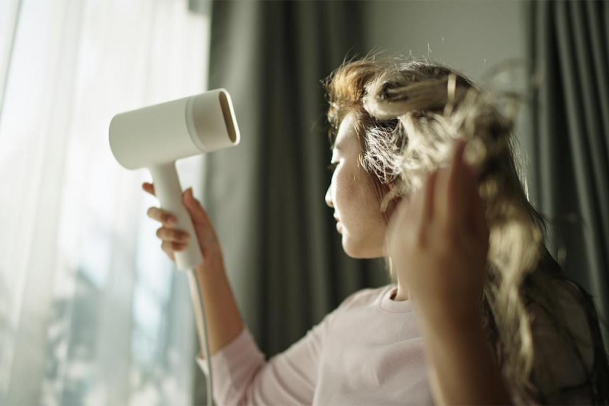 una chica secándose el pelo con un secador en casa.