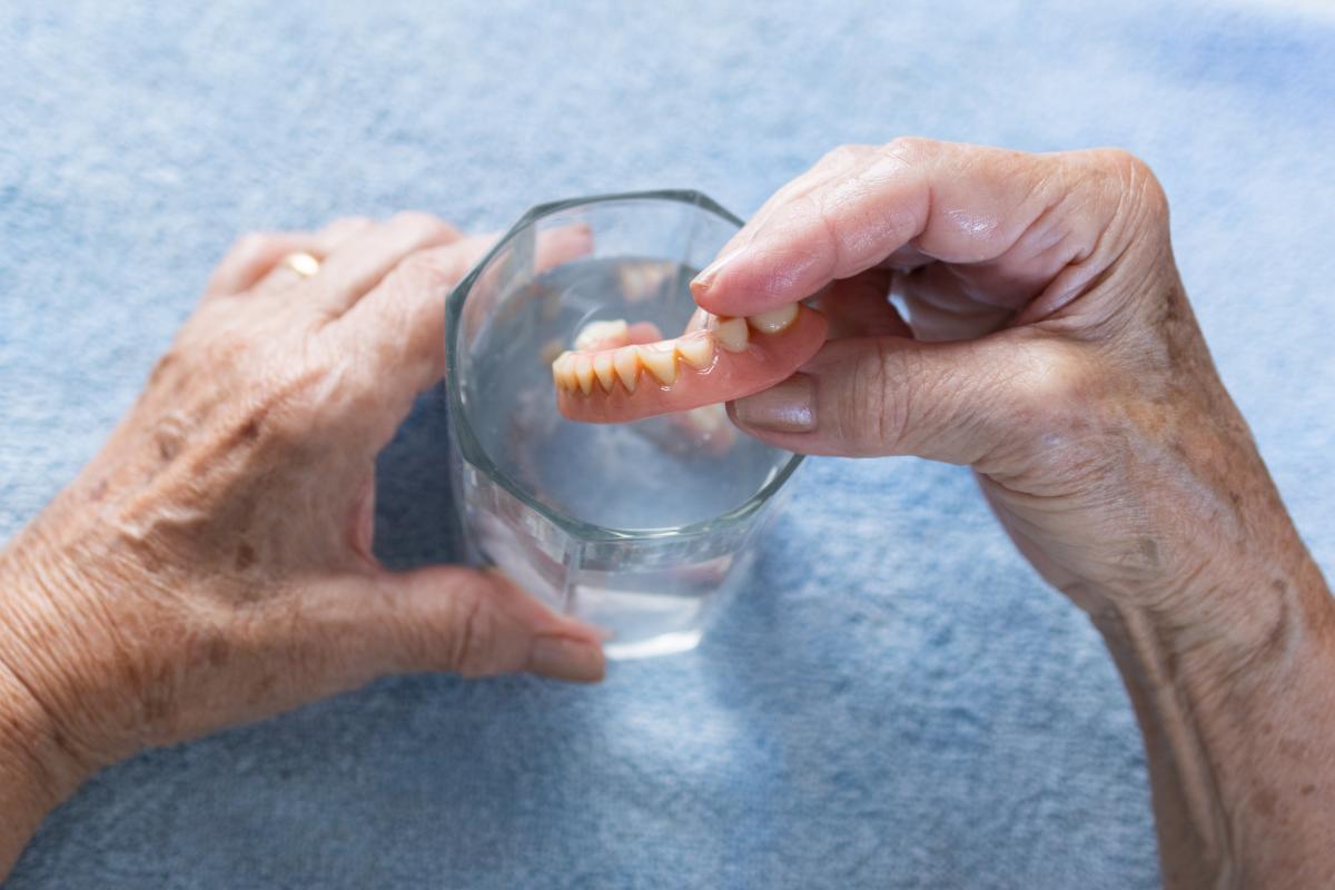 Una mujer metiendo su dentadura postiza en un vaso.