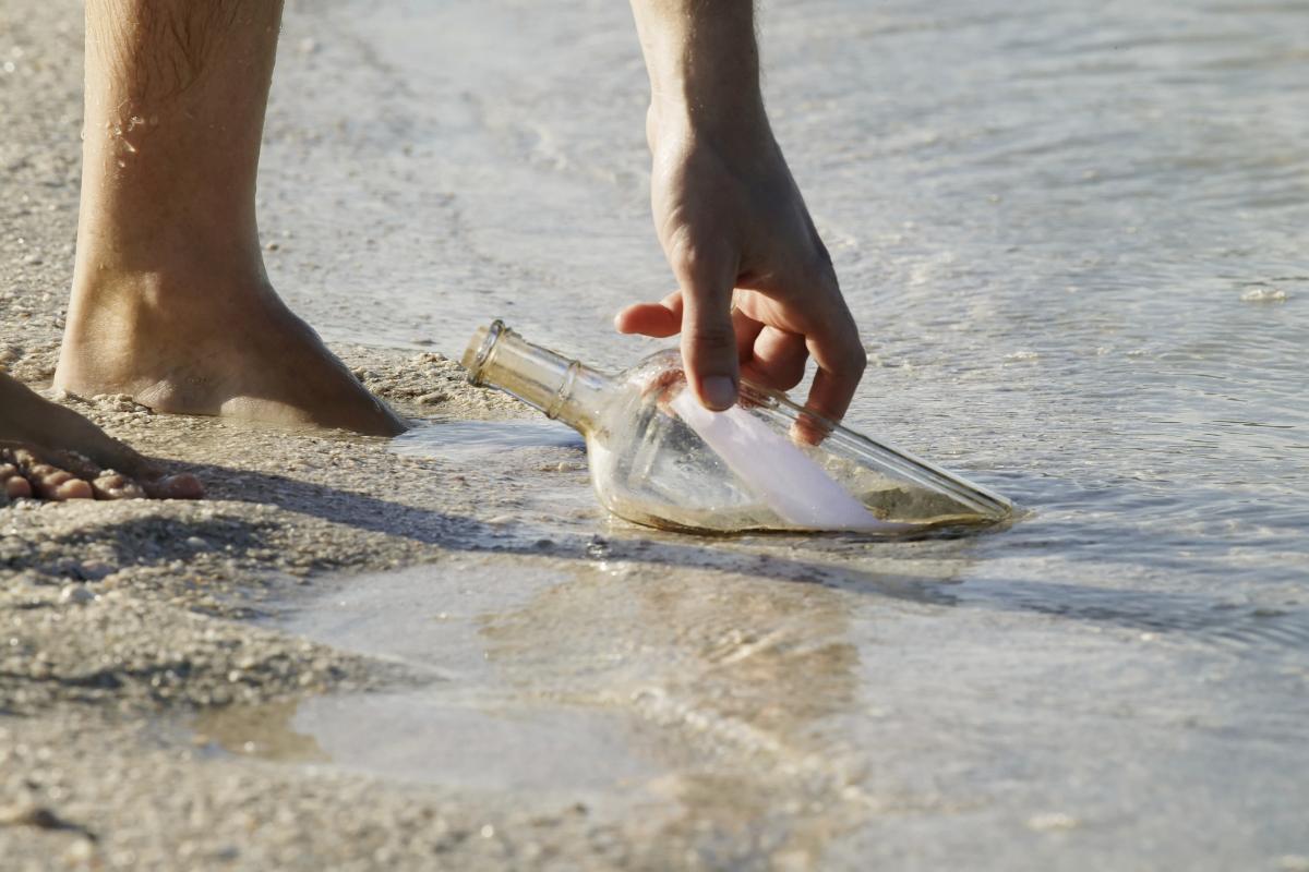 Una persona recogiendo una botella con un mensaje, en una imagen de archivo